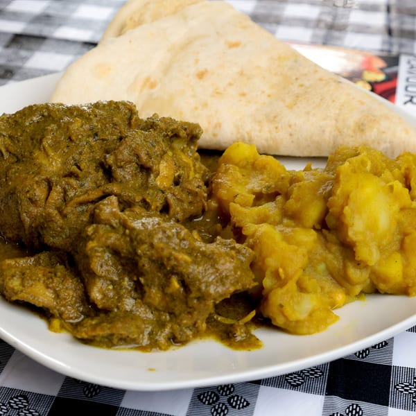 A Caribbean meal with green curry chicken, mashed yellow potatoes, and flatbread on a white plate.