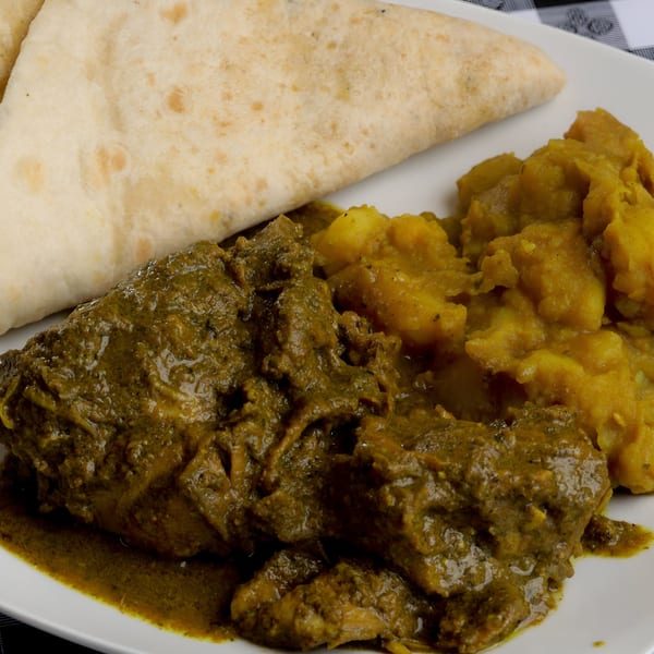 Curried chicken and potatoes with a folded flatbread on a white plate.