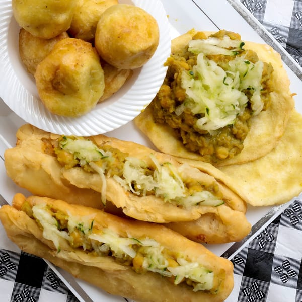 A plate of Caribbean doubles with chickpea curry and cucumber, alongside fried dumplings.